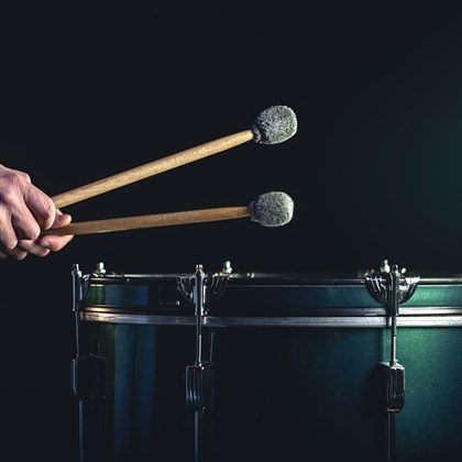 man plays musical percussion instrument with sticks dark background